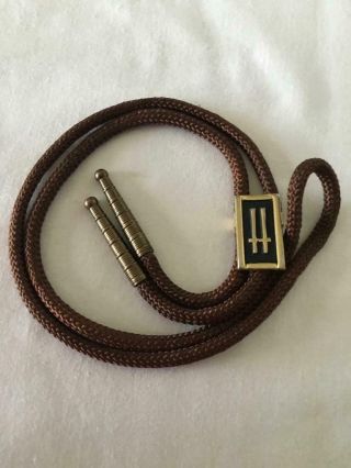 Bolo Tie With “h” Slide In Black And Gold Metal Cords Have Antique Gold Tips